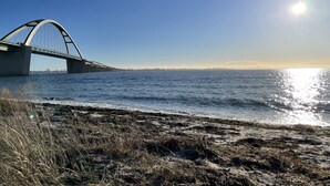 Un pont enjambant une étendue d’eau, avec un ciel dégagé et la lumière du soleil se reflétant sur l’eau.