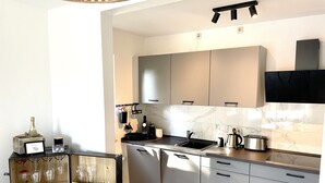 Une cuisine moderne avec des meubles gris, un évier en acier inoxydable et un plan de travail noir. On y trouve un présentoir en bois avec des verres à vin et une bouteille de champagne.