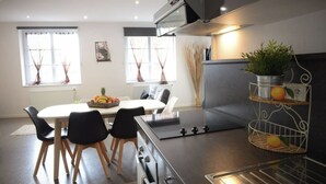 A modern kitchen with a central island, black chairs, a dining table, and a fruit basket. - L'ombre Dieppoise - Dieppe (Dieppe)