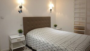 A bedroom with a tufted headboard, two bedside tables with lamps, a white bedspread, and a white shelving unit. - L'ombre Dieppoise - Dieppe (Dieppe)