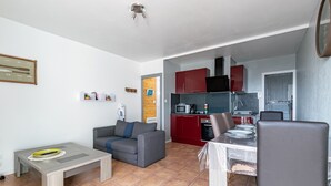 A compact living space with a grey sofa, a small dining table, and a kitchenette area with red cabinets.