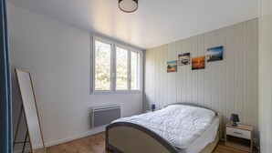 A bedroom with a bed, a nightstand, a lamp, a window, and wall-mounted pictures.