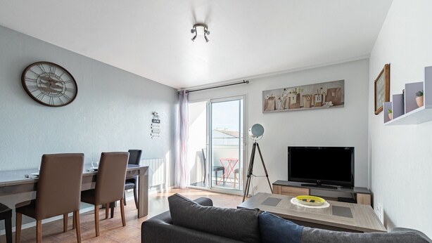 A modern living room with a sofa, dining table, chairs, a TV, and a large window.