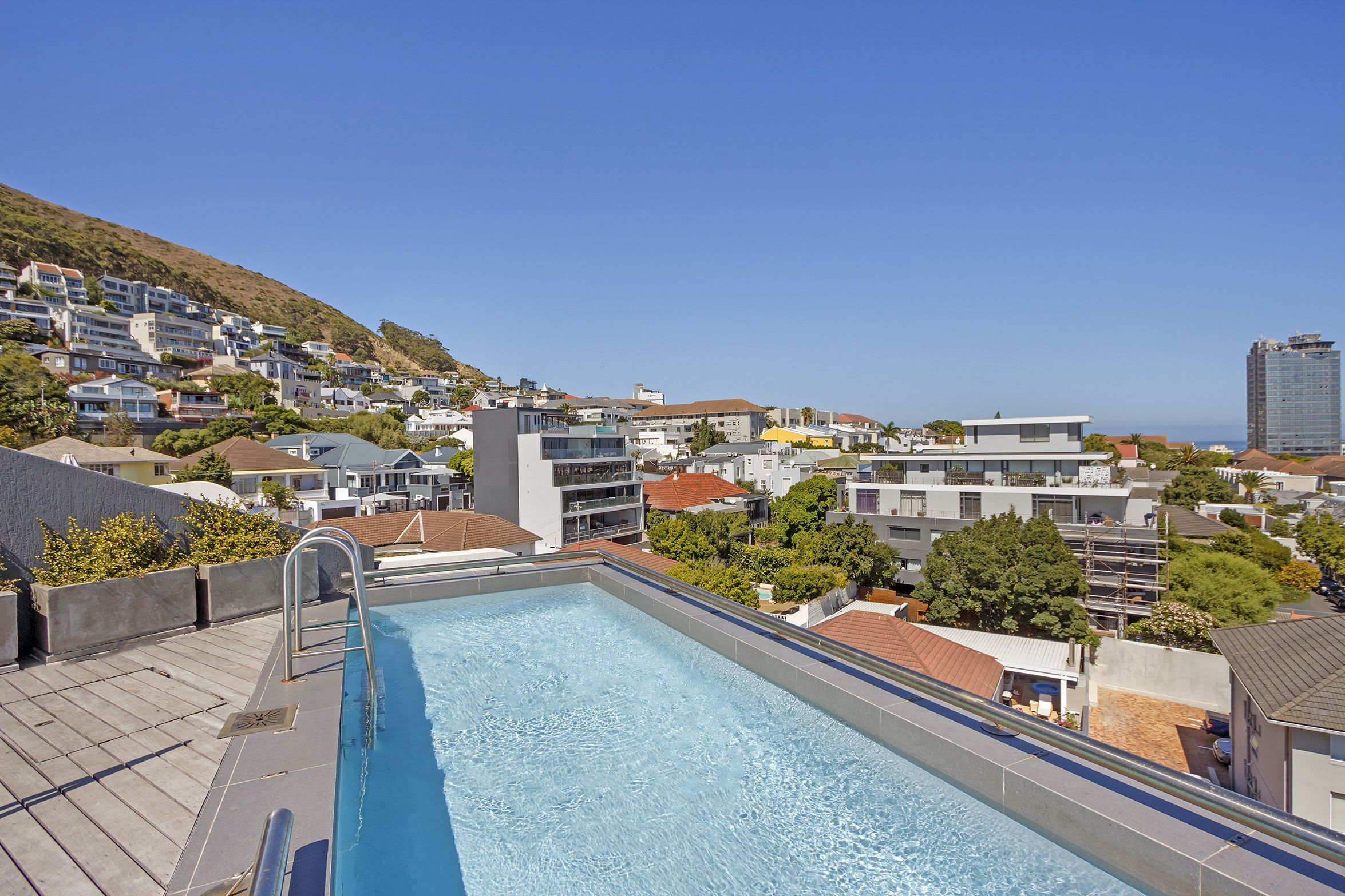 A rooftop swimming pool with a clear view of a hillside residential area and a distant building.