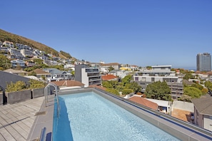 A rooftop swimming pool with a clear view of a hillside residential area and a distant building.