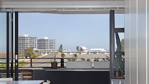A balcony with a table and chairs, potted plants, and a view of buildings. - Nine On S 3E (Cape Town)