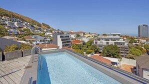 A rooftop swimming pool with a clear view of a hillside residential area and a distant building. - Nine On S 3E (Cape Town)