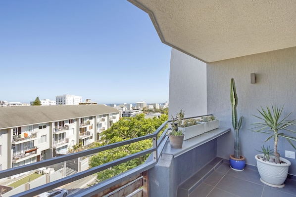A balcony with potted plants, a railing, and a view of buildings and greenery.