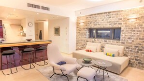 A modern living room with a stone wall, a sofa, a coffee table, and a bar area with stools. - Bright and Clean Rothchild Quarter (Tel Aviv)