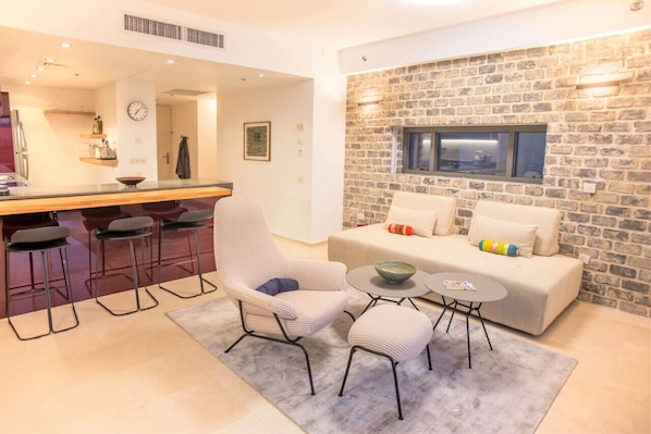 A modern living area with a stone wall, a sofa, a chair, a small table, and a kitchen area with bar stools.