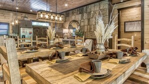 A rustic dining area with wooden tables and chairs, a chandelier, and a stone wall.