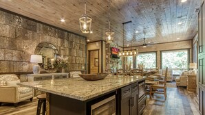 A spacious kitchen with a large island, wooden ceiling, and a stone accent wall.