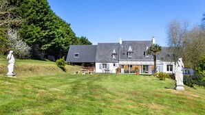 Ein großes, zweistöckiges Haus mit gepflegtem Rasen, Sitzgelegenheiten im Freien und Statuen.