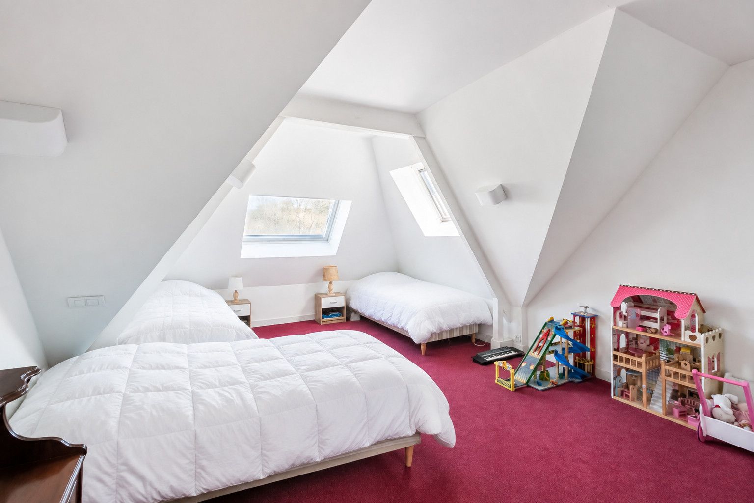 Ein Schlafzimmer mit zwei Betten, einem Dachfenster, einem Spielhäuschen und einem roten Teppich.