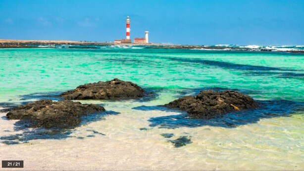Eine Küstenlandschaft mit einem Leuchtturm, klarem türkisblauem Wasser und Felsformationen.