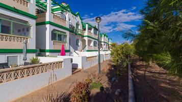 A row of white buildings with green accents and balconies, a paved walkway, and some landscaping.