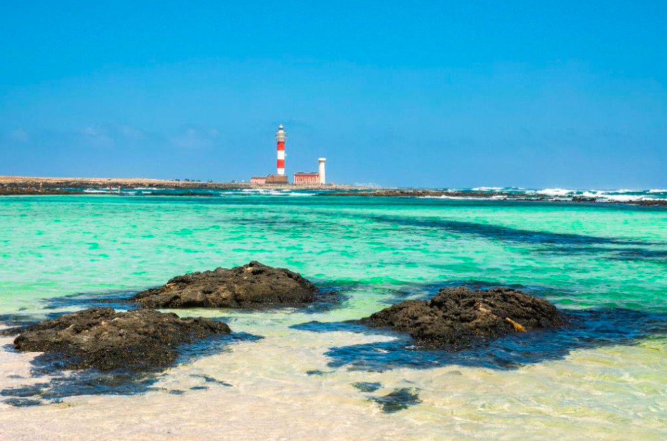 A coastal scene with a lighthouse, clear turquoise waters, and rocky outcrops.