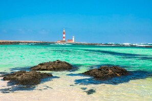 A coastal scene with a lighthouse, clear turquoise waters, and rocky outcrops. - HomeForGuest Spacious flat with terrace and swimming pool (Antigua - Fuerteventura)