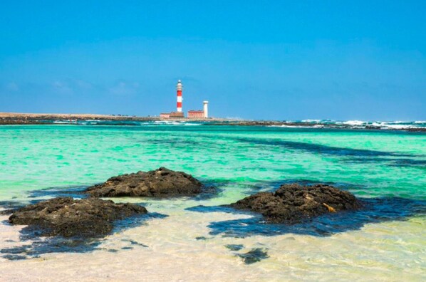 Een kustlandschap met een vuurtoren, helder turquoise water en rotsachtige rotsformaties.