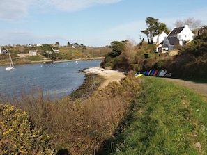 Blick auf die Küste mit einem Sandstrand, einem Grasweg und Häusern im Hintergrund.