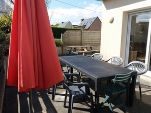 Eine Terrasse im Freien mit Tisch und Stühlen, einem roten Sonnenschirm und einem Holzzaun im Hintergrund.