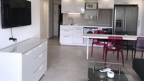 Een moderne keuken met witte kasten, een ingebouwde magnetron, een roestvrijstalen koelkast en een glazen eettafel met rode stoelen.