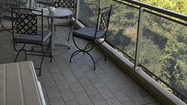 Een overdekt terras met tafels en stoelen, met uitzicht op groen en gebouwen.