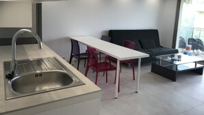 Een moderne keuken met een RVS spoelbak, een witte eettafel, rode stoelen en een zwarte bank.