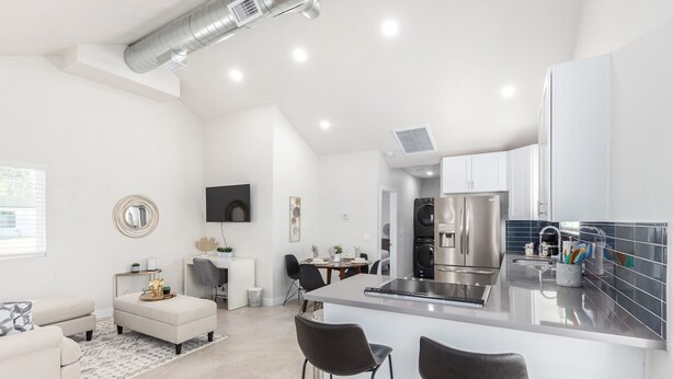 Una cocina moderna con una isla central, electrodomésticos de acero inoxidable y un comedor con mesa y sillas blancas.
