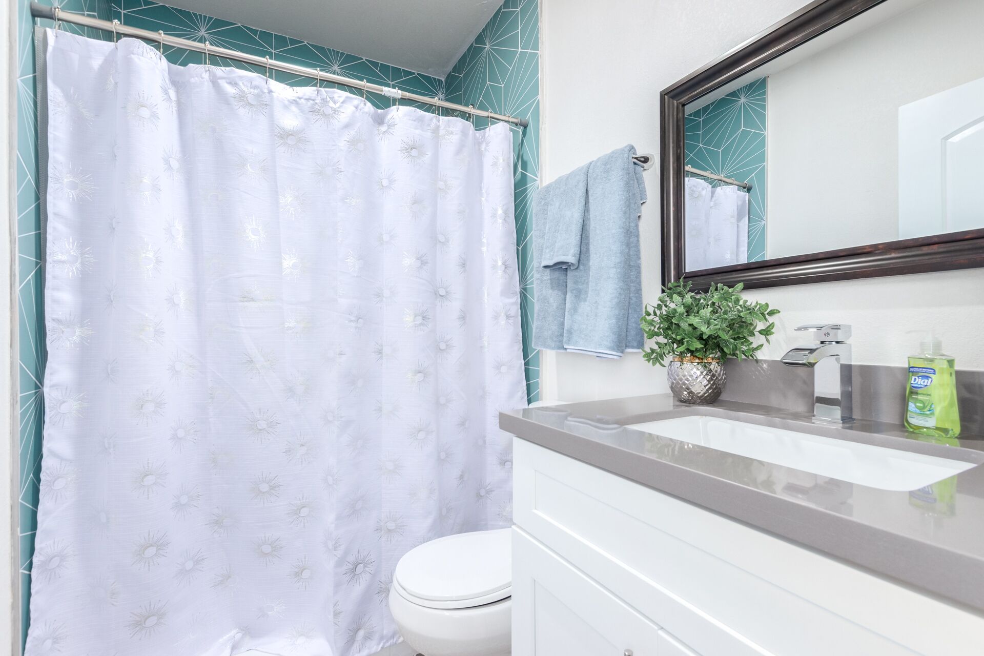 A bathroom with a white shower curtain, a white toilet, a sink with a mirror, and a potted plant.