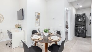Una cocina moderna con lavadora y secadora integradas, un comedor con una mesa redonda y sillas, y un televisor montado en la pared.