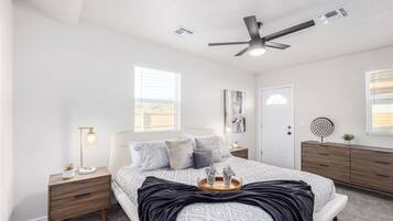 Ein Schlafzimmer mit Bett, Nachttischen, Deckenventilator, Tür und Fenster.