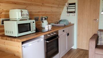 Cocina pequeña con microondas, tostadora y cafetera sobre la encimera, armarios de madera y una puerta con un cartel motivacional.