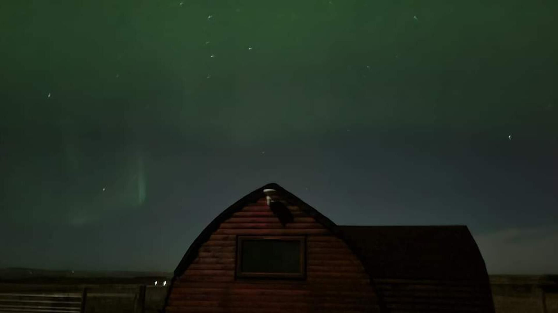Une cabane en bois, dotée d’un toit triangulaire et d’une petite fenêtre, se dressant sur fond de ciel nocturne parsemé d’étoiles.