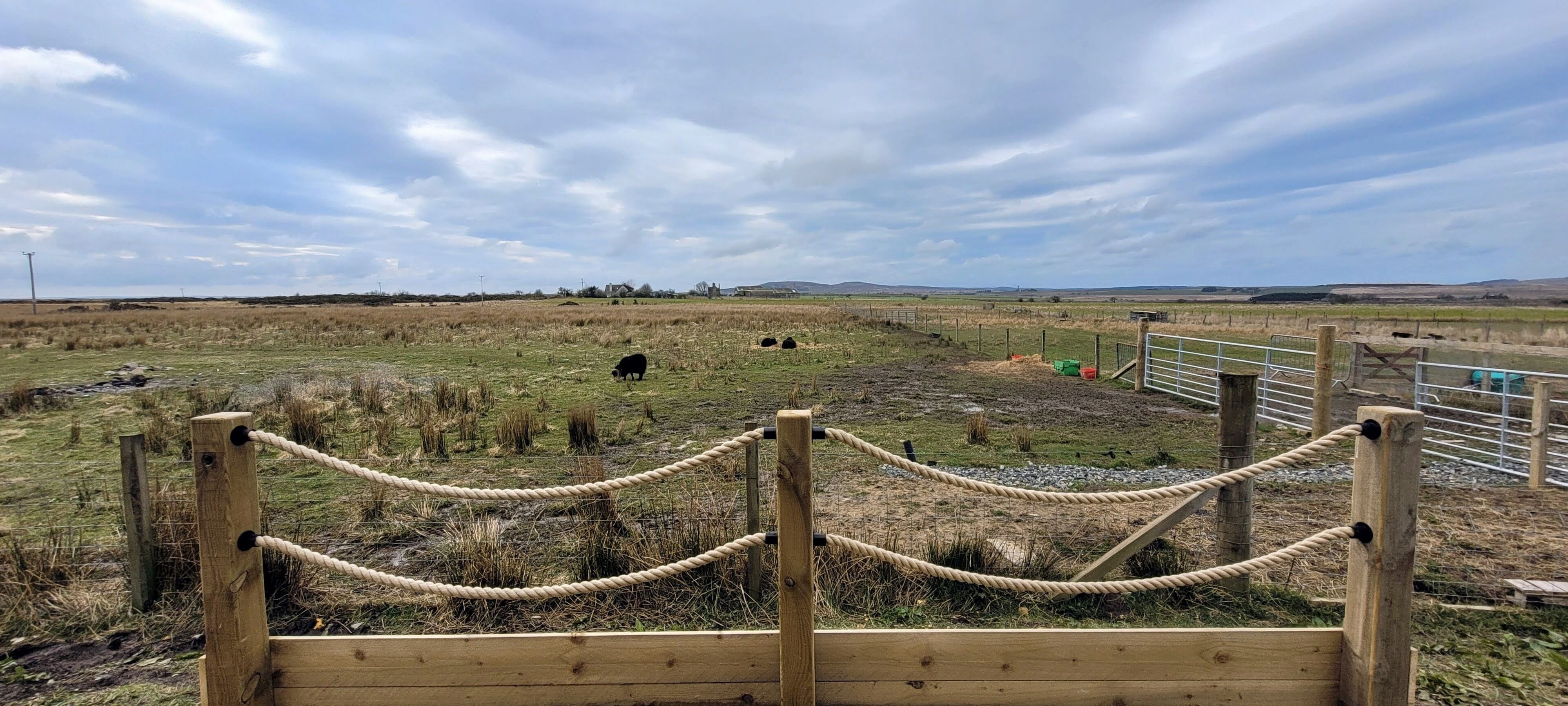 A fenced area with a rope barrier, a wooden gate, and a landscape with grazing animals.