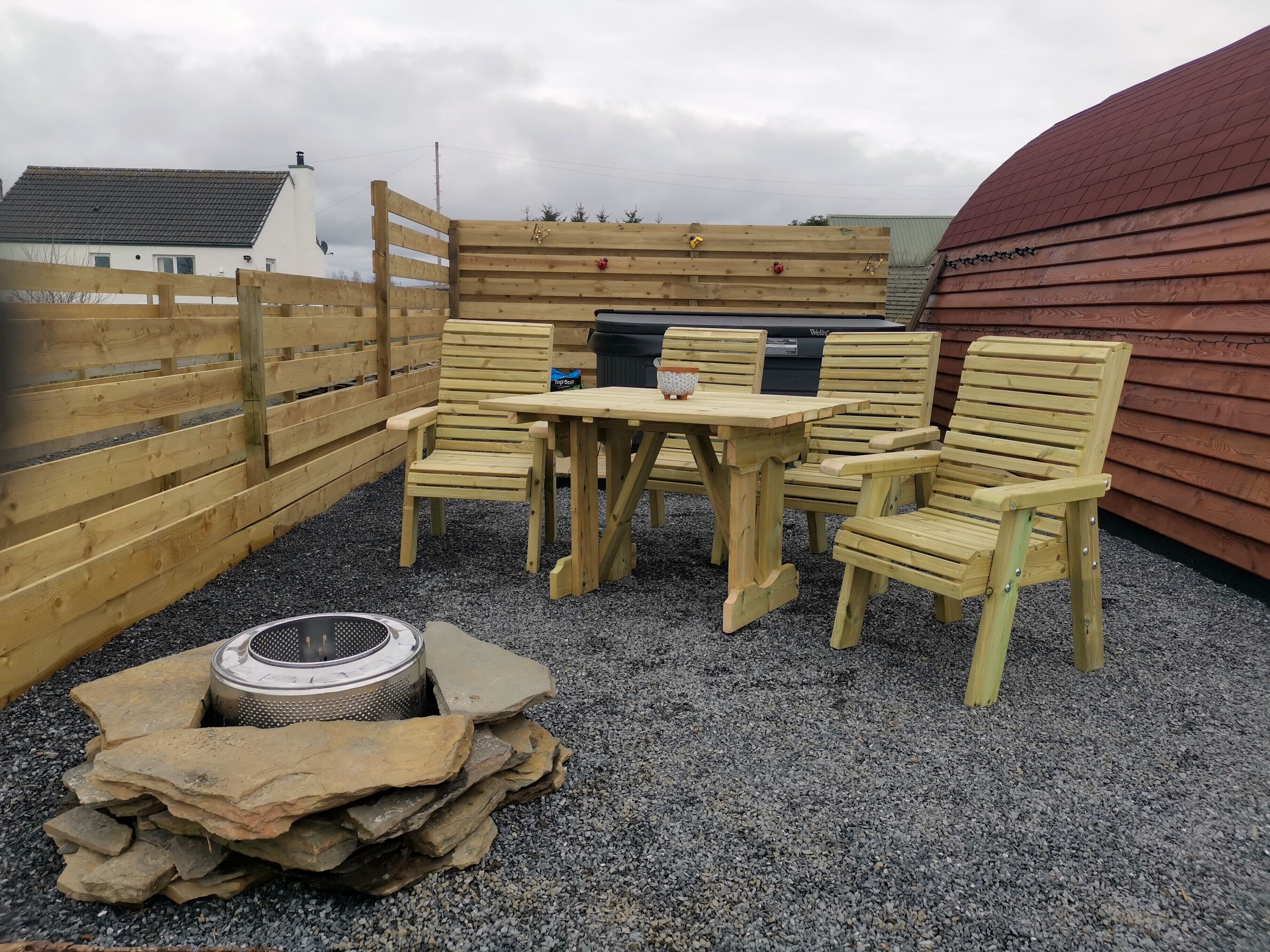 A wooden outdoor seating area with a table and chairs, a barbecue grill, and a fire pit.