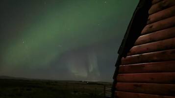 Una vista dell'aurora boreale ammirata dalla finestra di una baita con facciata in legno.