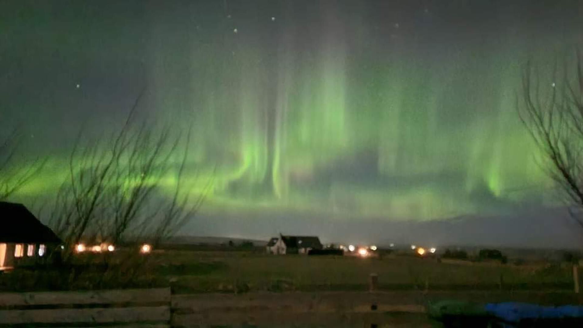 A rural landscape at night with the Northern Lights visible in the sky.