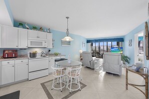 A modern kitchen with white cabinets, a microwave, and a dining area with a round table and chairs. - Waterfront Condo in Anglers Cove | Pools & Spas (Marco Island)