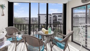 Un balcon agrémenté de meubles en osier, une table avec une serviette et des bouteilles, et une vue sur les bâtiments en arrière-plan.