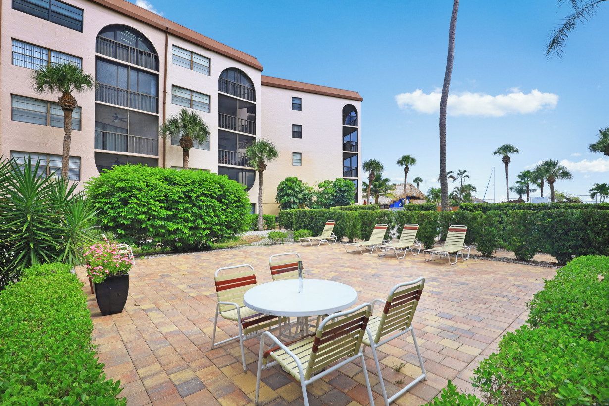A courtyard with a round table and chairs, surrounded by palm trees and a building with large windows.