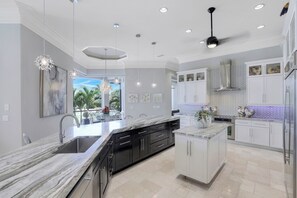 A modern kitchen with a central island, white cabinetry, and pendant lighting. - Waterfront Home | Infinity Pool, Spa & Outdoor Fireplace (Marco Island)