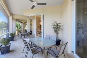 A spacious patio with a round table and chairs, surrounded by potted plants and a ceiling fan.
