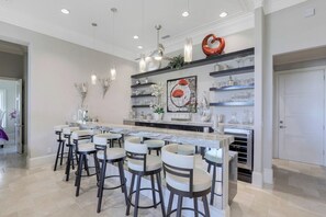 A modern kitchen with a central island, bar stools, pendant lighting, and decorative shelves.