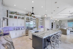A modern kitchen with white cabinetry, a central island with bar stools, and pendant lighting. - Waterfront Home | Infinity Pool, Spa & Outdoor Fireplace (Marco Island)