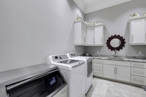 A laundry room with a washer and dryer, white cabinets, a marble countertop, and a decorative mirror.