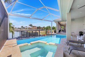 A swimming pool with a glass enclosure, lounge chairs, and a view of the surrounding landscape. - Waterfront Home | Infinity Pool, Spa & Outdoor Fireplace (Marco Island)