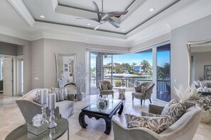 A spacious living room with a large glass door leading to a balcony, a ceiling fan, and a modern coffee table. - Waterfront Home | Infinity Pool, Spa & Outdoor Fireplace (Marco Island)
