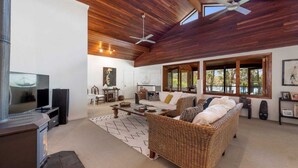 A spacious living room with a high ceiling, wooden beams, a large sofa, a television, and a dining area. - Lakeside Lodge - Fabulous Waterfront Holiday (Laurieton)