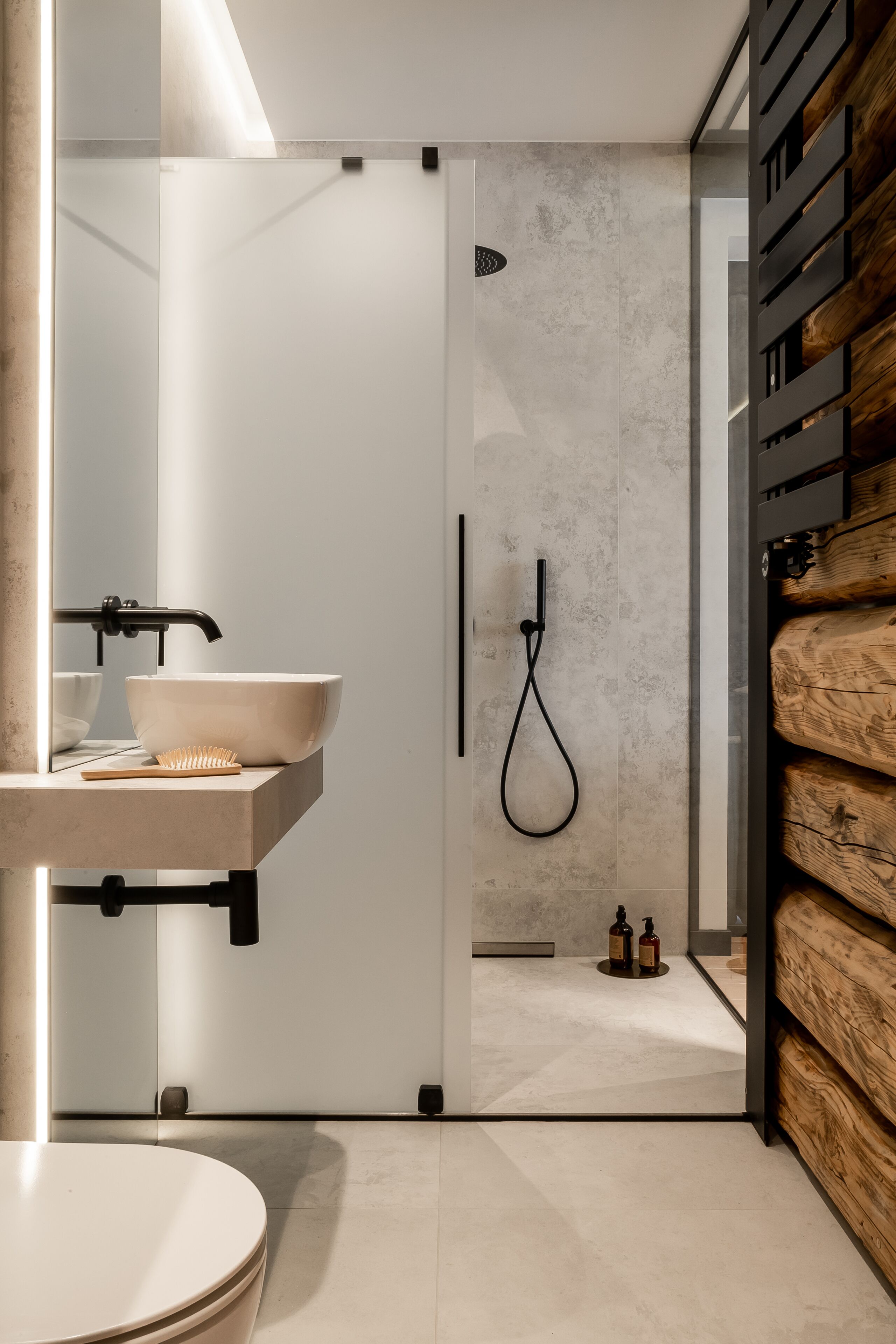 Ein modernes Badezimmer mit einer in Glas eingefassten Dusche, einem weißen Waschbecken mit einer Holzbürste und einer Holzvertäfelung.